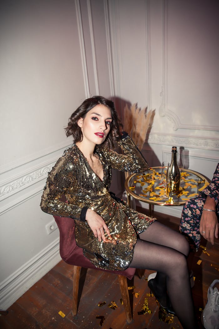 Woman in gold dress sitting at a party table with champagne, celebrating an elegant occasion.