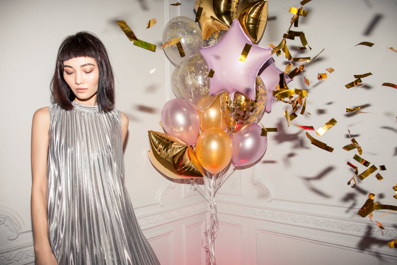 Stylish woman in silver dress celebrating birthday with balloons indoors.